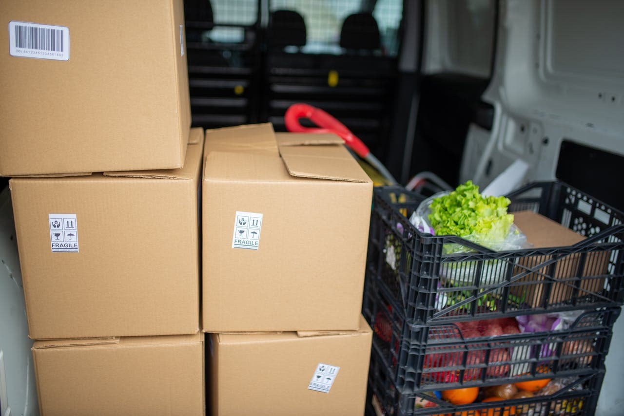 Cardboard boxes and fresh produce being prepared for delivery in a van, highlighting logistics and farm-to-table movement.